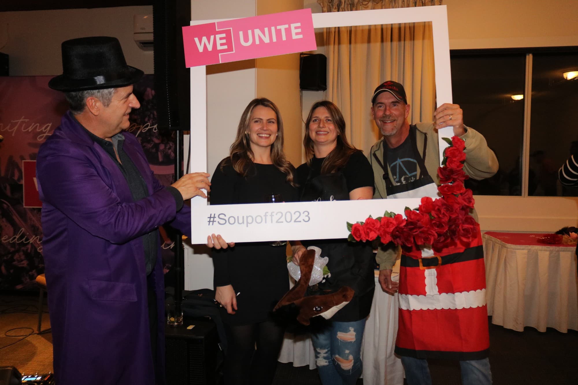 Guests posing in the rose-trimmed WE Unite #Soupoff2023 photo frame, joined by someone in a purple coat and top hat